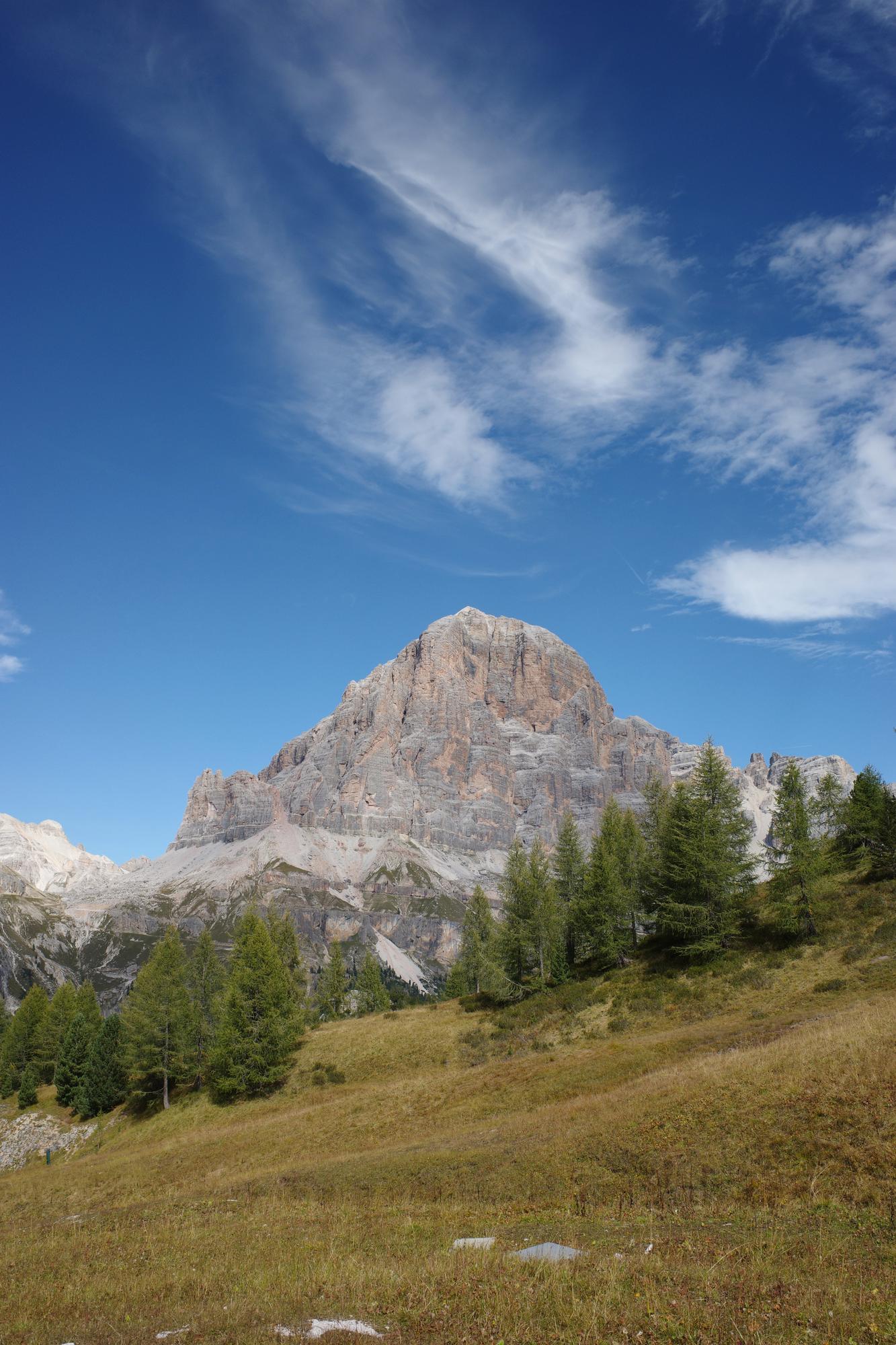A pyramidal Dolomite peak rising above a golden autumn meadow and larch trees